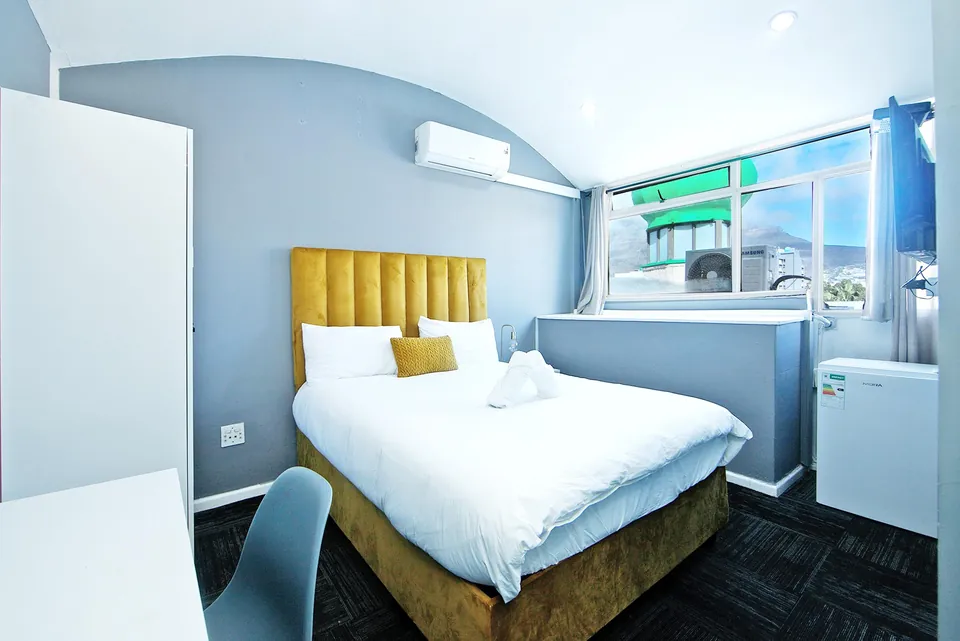Queen bed with yellow headboard, air conditioning and a window